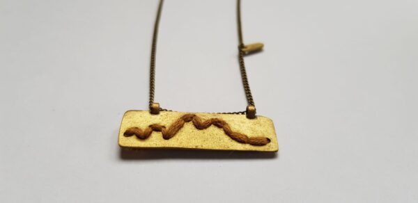 Close-up of rectangular brass pendant with Mustard cotton mountain ridgeline detail on brass chain