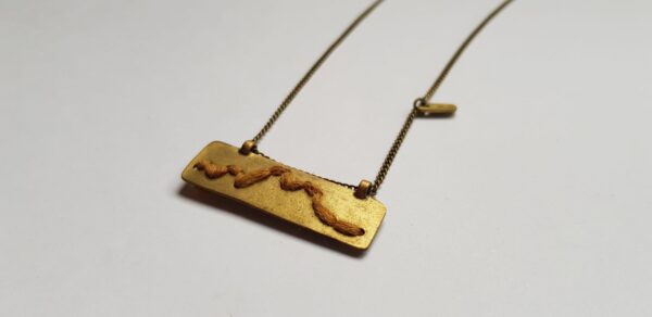 Left angle of rectangular brass pendant with Mustard cotton mountain ridgeline detail on brass chain