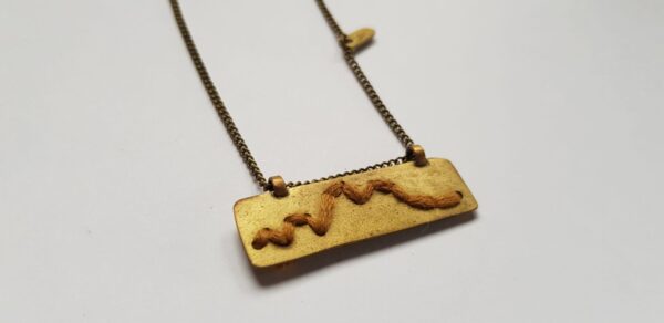 Right angle of rectangular brass pendant with Mustard cotton mountain ridgeline detail on brass chain