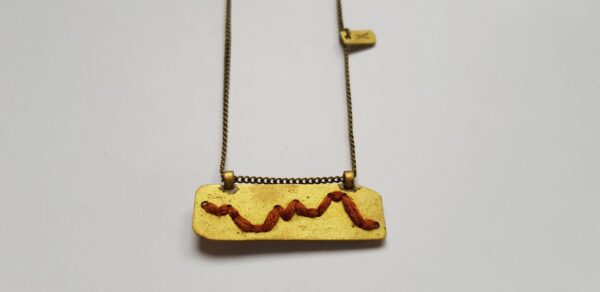 Close-up of rectangular brass pendant with Rust colour cotton mountain ridgeline detail on brass chain