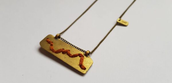Left angle of rectangular brass pendant with Rust colour cotton mountain ridgeline detail on brass chain