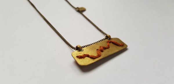 Right angle of rectangular brass pendant with Rust colour cotton mountain ridgeline detail on brass chain