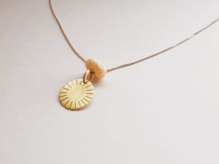 Brass disc pendant with hand-cut lines and off-white decorative carved shell bead on silver chain